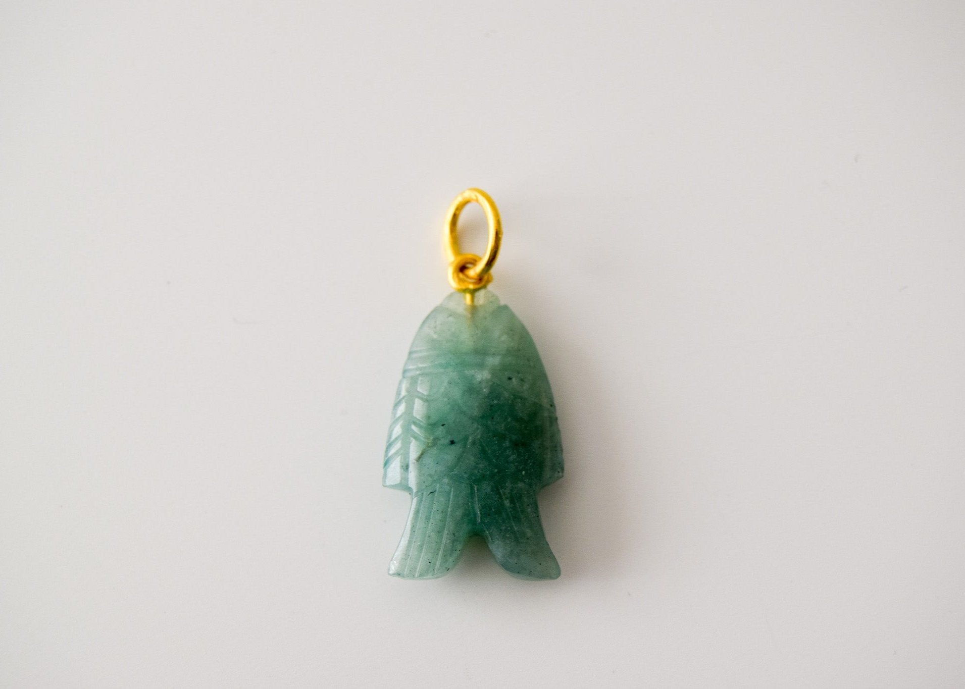 Intricately detailed, this versatile amazonite fish charm features a delicate fish design carved from amazonite gemstone, with the pendant ring made of gold plated material, it is  perfect for various jewelry creations, displayed on a neutral background.