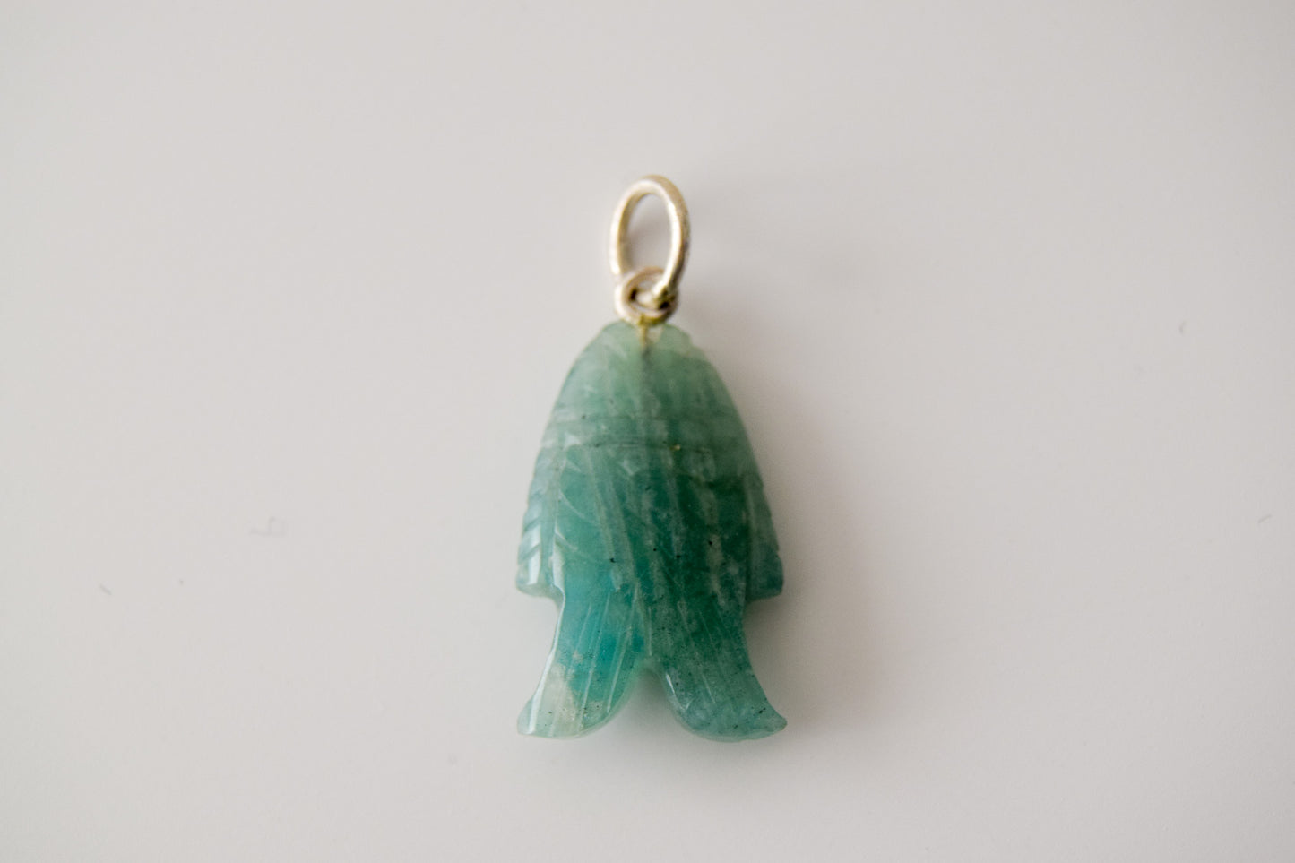 Intricately detailed, this versatile amazonite fish charm features a delicate fish design carved from amazonite gemstone, with the pendant ring made of silver plated material, it is  perfect for various jewelry creations, displayed on a neutral background.