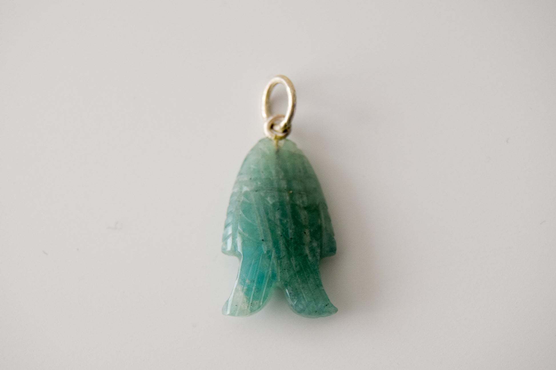 Intricately detailed, this versatile amazonite fish charm features a delicate fish design carved from amazonite gemstone, with the pendant ring made of silver plated material, it is  perfect for various jewelry creations, displayed on a neutral background.