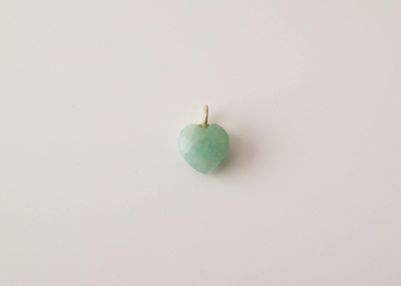 Intricately detailed, this versatile amazonite heart shaped charm features a delicate heart design carved from amazonite gemstone, with the pendant ring made of gold plated material, it is  perfect for various jewelry creations like a necklace or earrings, displayed on a neutral background.