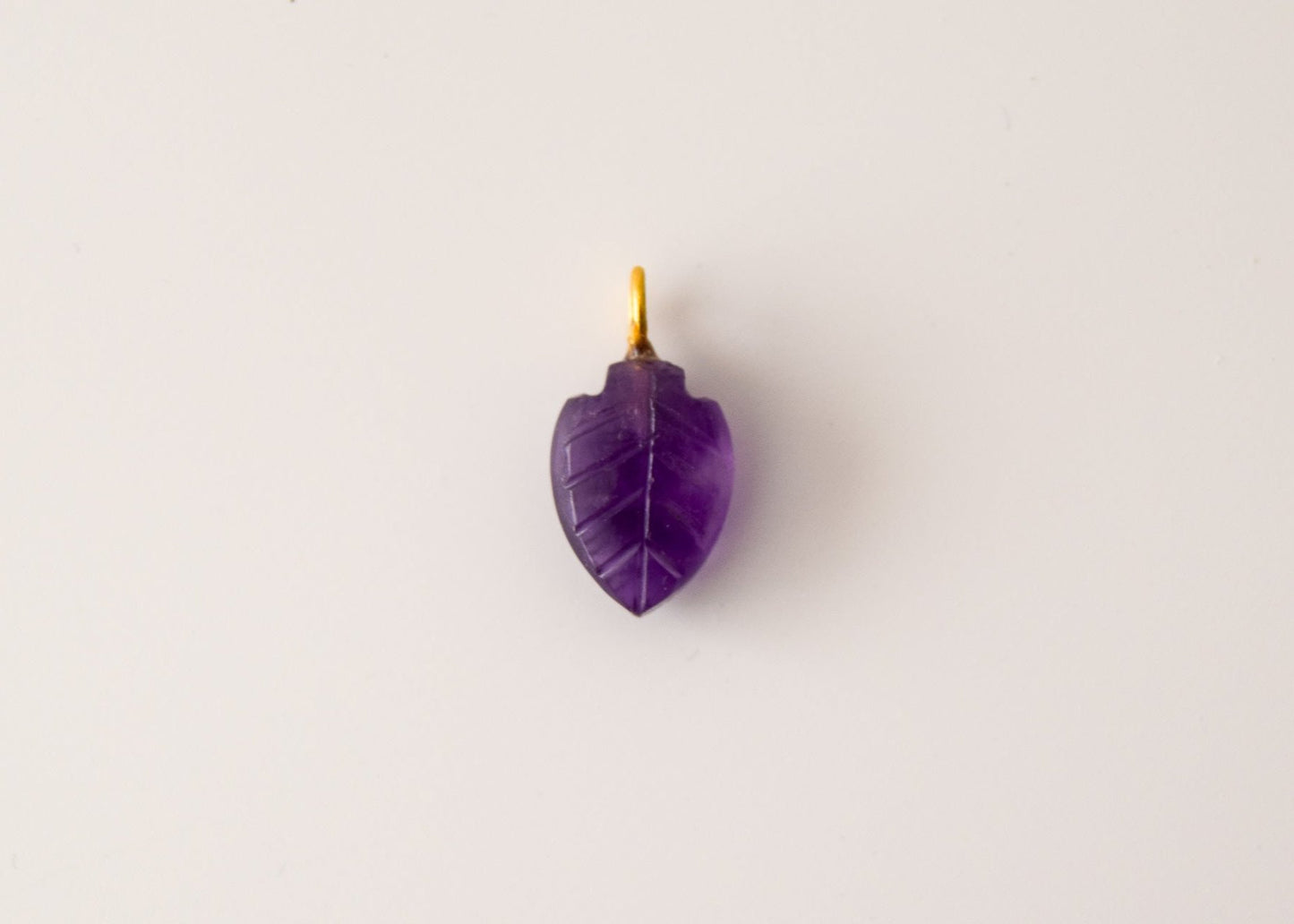 Intricately detailed, this versatile amethyst leaf shaped charm features a delicate leaf design carved from amethyst gemstone, with the pendant ring made of gold plated material, it is  perfect for various jewelry creations like a necklace or earrings, displayed on a neutral background.