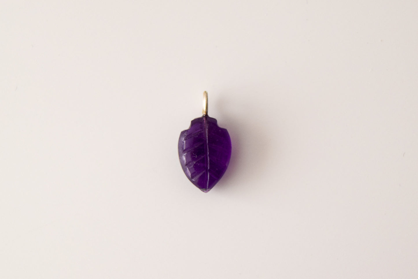 Intricately detailed, this versatile amethyst leaf shaped charm features a delicate leaf design carved from amethyst gemstone, with the pendant ring made of silver plated material, it is  perfect for various jewelry creations like a necklace or earrings, displayed on a neutral background.