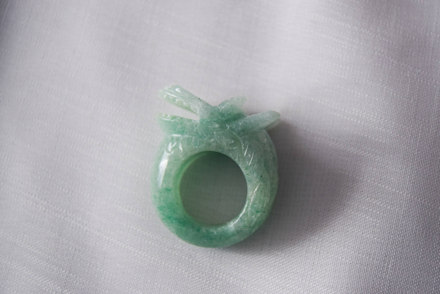 Aventurine stone ring with carved and engraved dragon on a white textile background