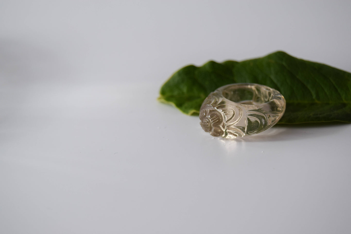 Clear Quartz stone ring with carved and engraved flower on a leaf stone background