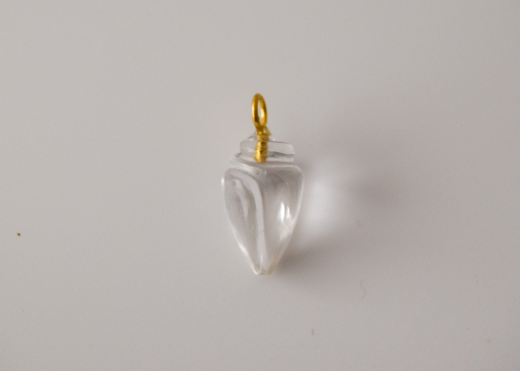 Intricately detailed, this versatile clear quartz conch shell charm features a delicate conch shell design carved from clear quartz gemstone, with the pendant ring made of gold plated material, it is  perfect for various jewelry creations like a necklace or earrings, displayed on a neutral background.