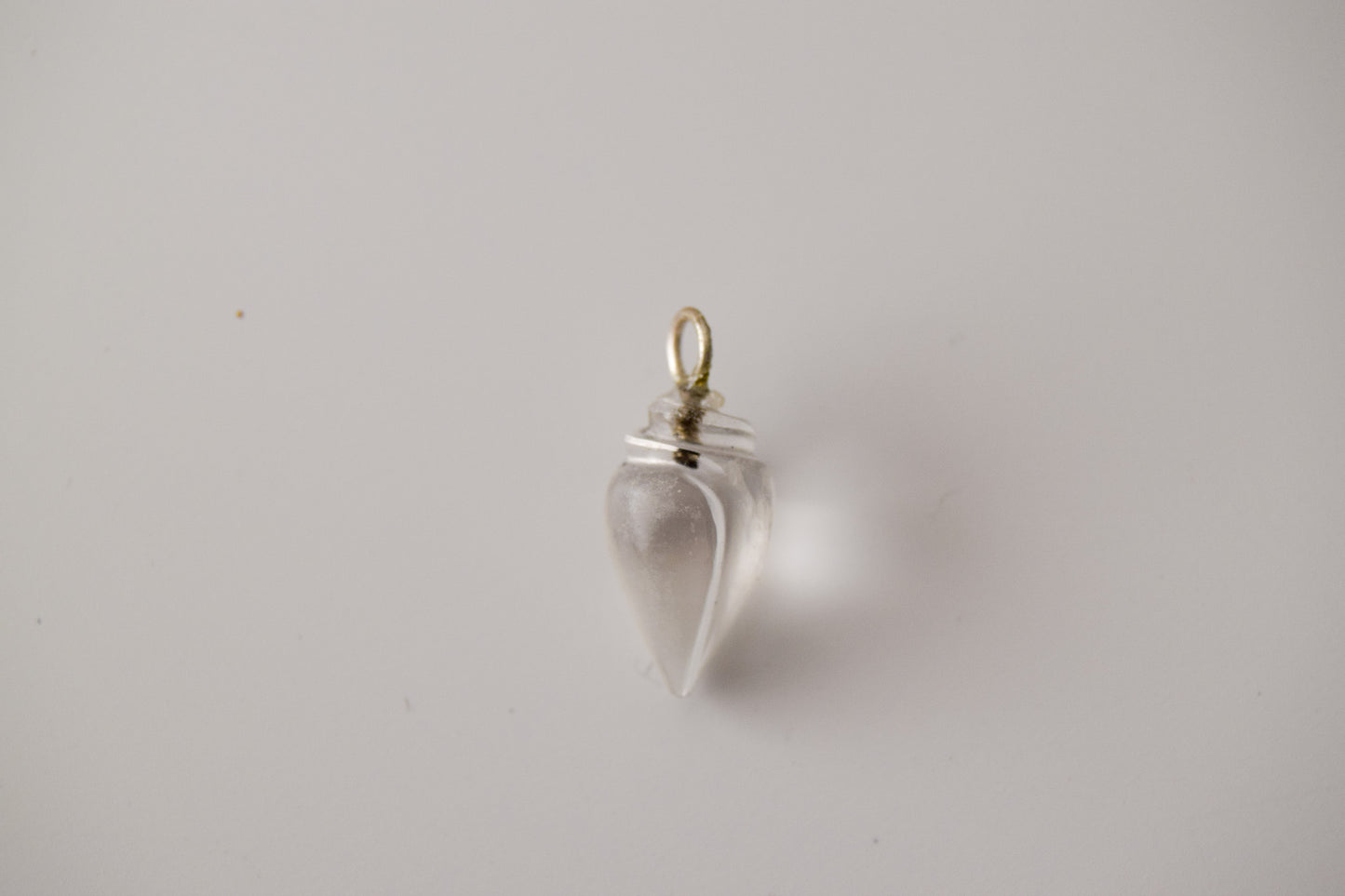 Intricately detailed, this versatile clear quartz conch shell charm features a delicate conch shell design carved from clear quartz gemstone, with the pendant ring made of silver plated material, it is  perfect for various jewelry creations like a necklace or earrings, displayed on a neutral background.