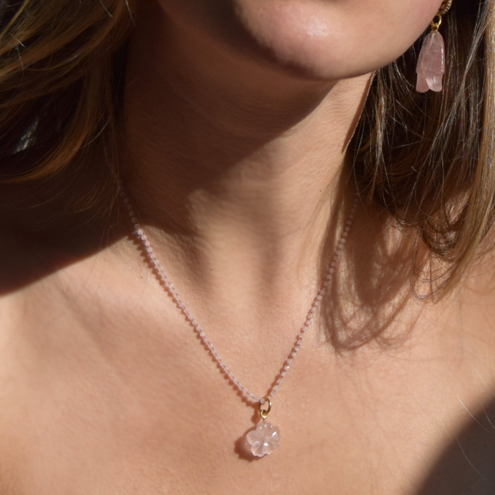 Close-up of a person wearing a delicate necklace with a pink pendant.