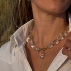Close-up of a person wearing a clear crystal necklace with a blurred natural background