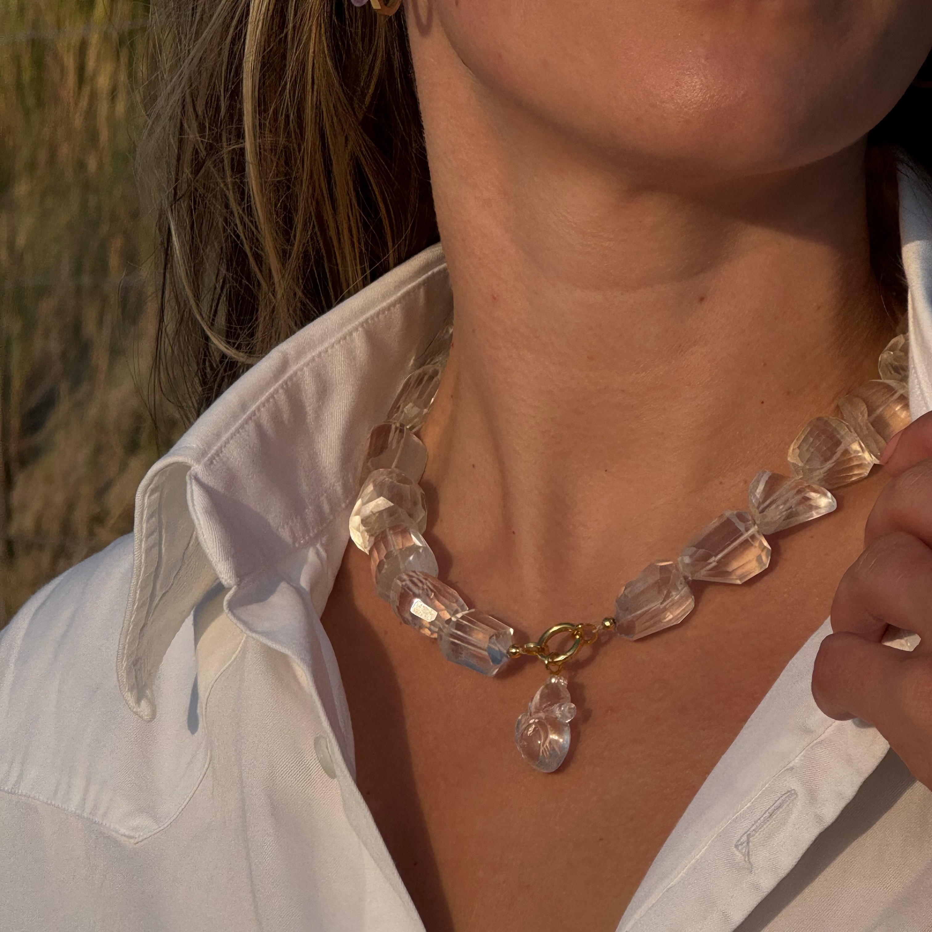 Close-up of a person wearing a clear crystal necklace with a blurred natural background
