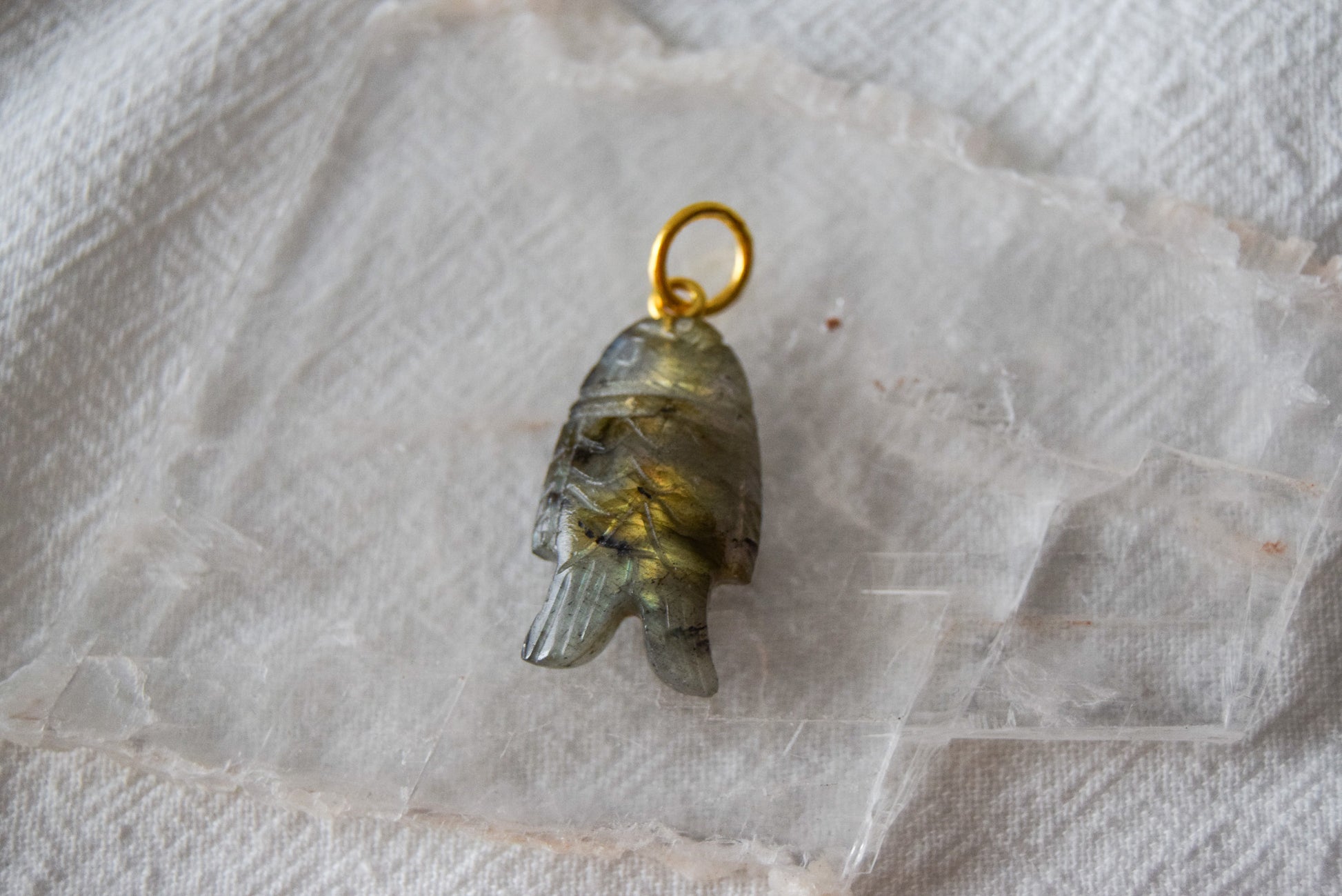 Intricately detailed, this versatile labradorite fish charm features a delicate fish design carved from labradorite gemstone, with the pendant ring made of gold plated material, it is  perfect for various jewelry creations like a necklace or earrings, displayed on a clear crystal background