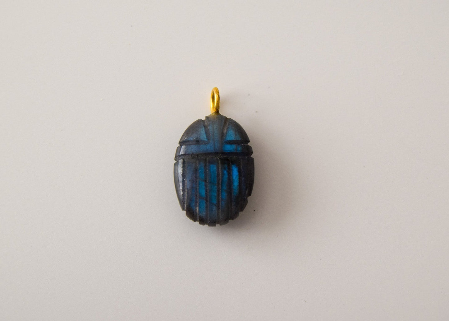 Intricately detailed, this versatile labradorite scarab charm features a delicate scarab design carved from labradorite gemstone, with the pendant ring made of gold plated material, it is  perfect for various jewelry creations like a necklace or earrings, displayed on a neutral background