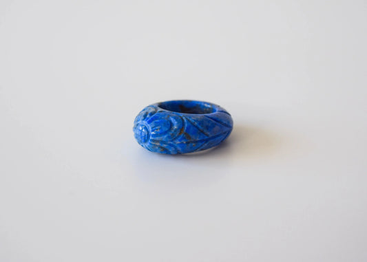 Lapis lazuli stone ring with carved and engraved flower on a neutral background