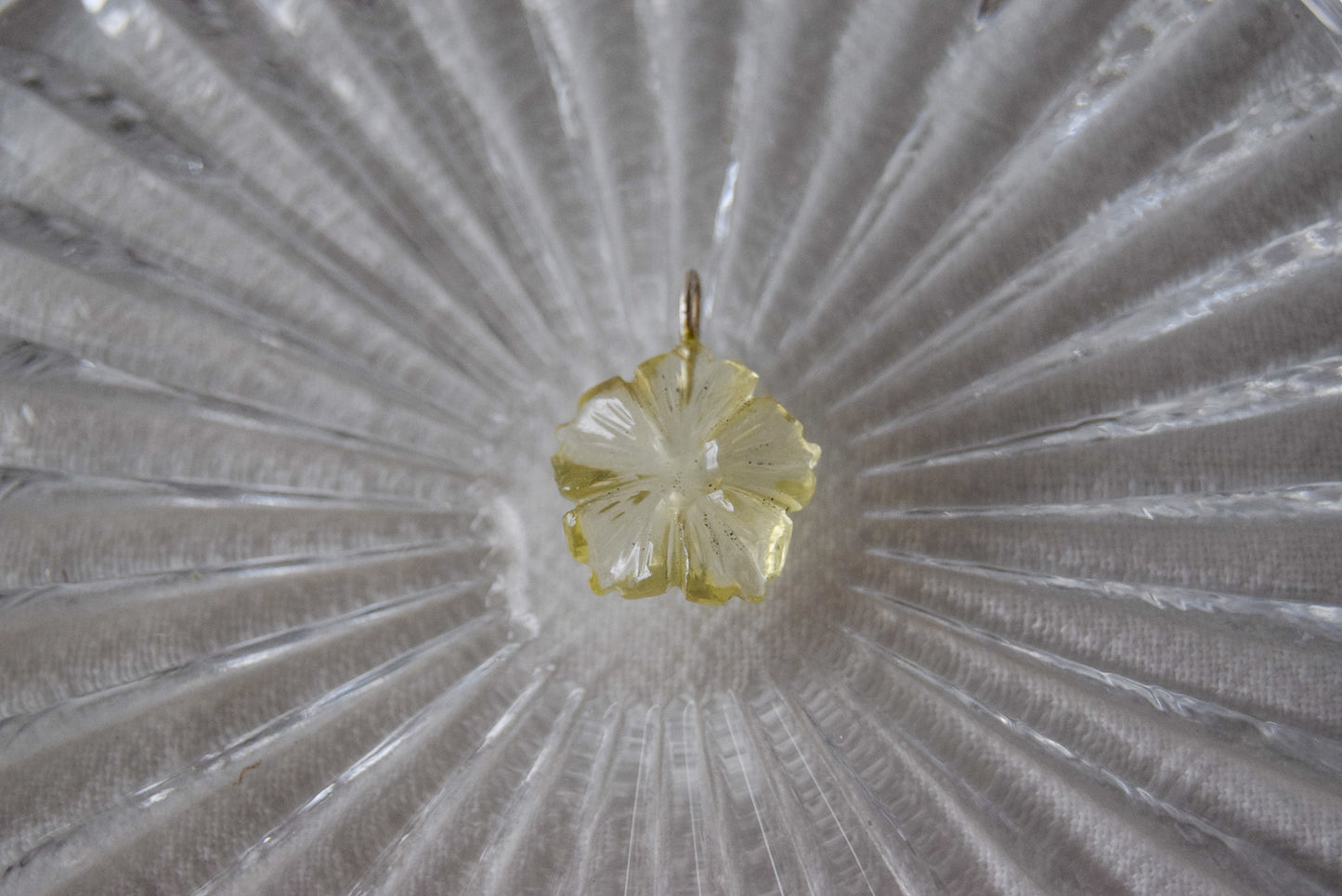 Intricately detailed, this versatile lemon quartz flower charm features a delicate flower design carved from lemon quartz gemstone, it is  perfect for various jewelry creations like a necklace or earrings, displayed on a crystal glass background