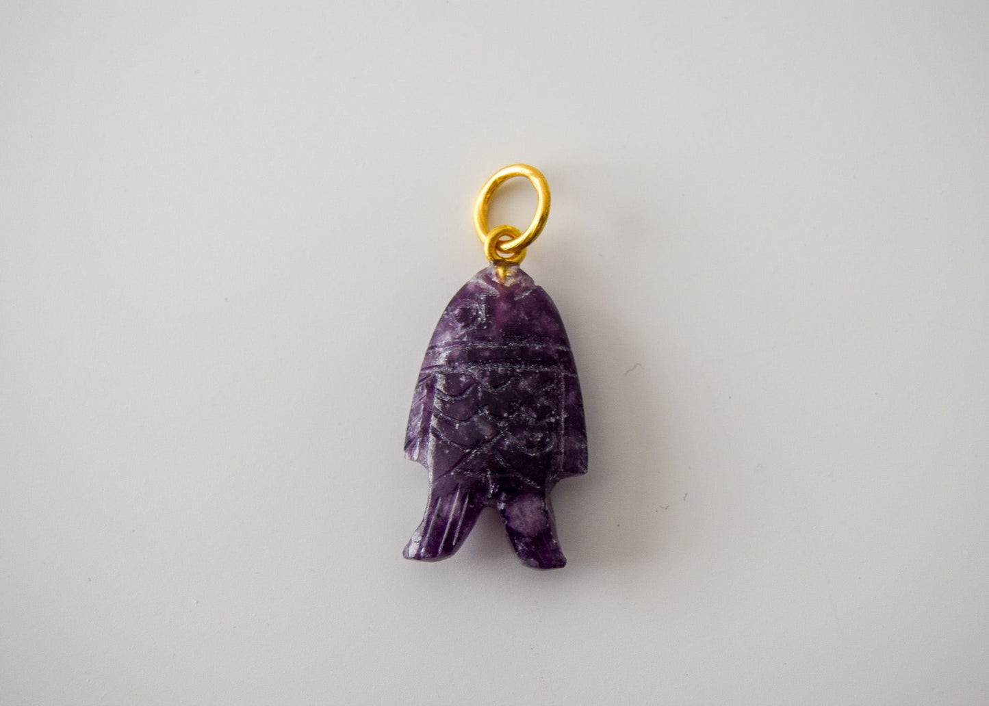 Intricately detailed, this versatile lepidolite fish charm features a delicate fish design carved from lepidolite gemstone, with the pendant ring made of gold plated material, it is perfect for various jewelry creations like a necklace or earrings, displayed on a neutral background