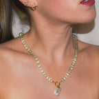 Close-up of a person wearing a delicate necklace with a clear pendant against a neutral background
